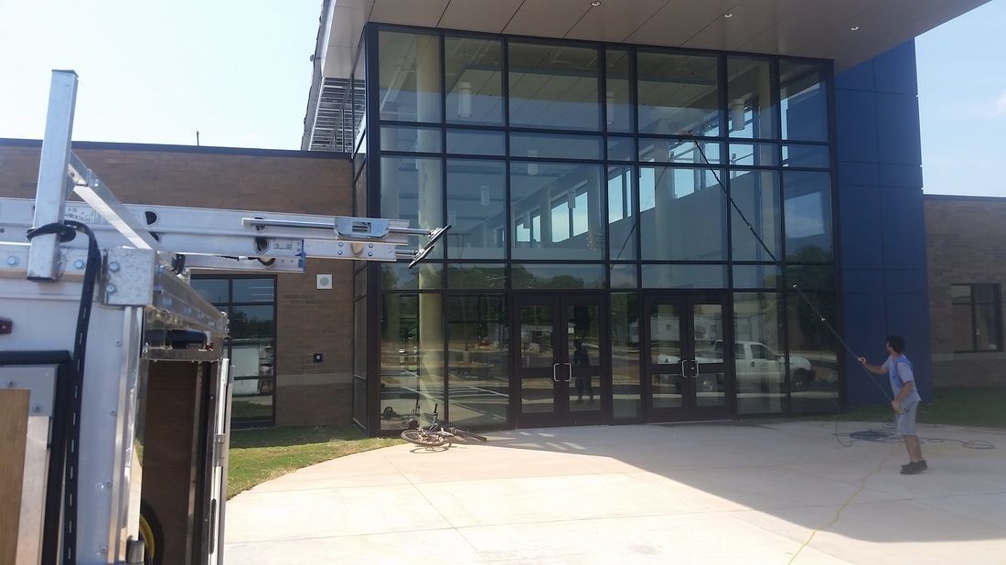 A service vehicle with a ladder rack is parked in front of a modern glass building entrance under a bright, sunny sky.