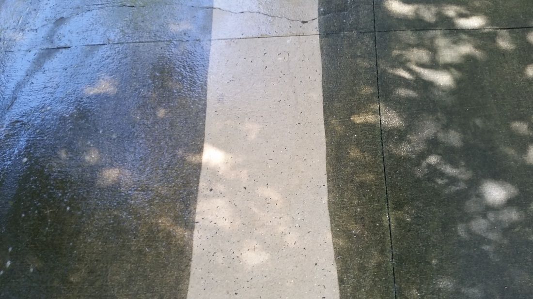 A section of concrete pavement showing a clean, white pressure-washed path between two darker, stained areas.