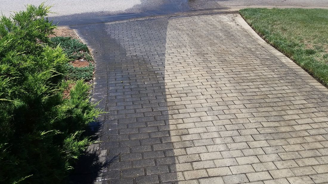 A partially cleaned stone driveway showing a sharp contrast between dark, dirty pavers and light, cleaned sections.