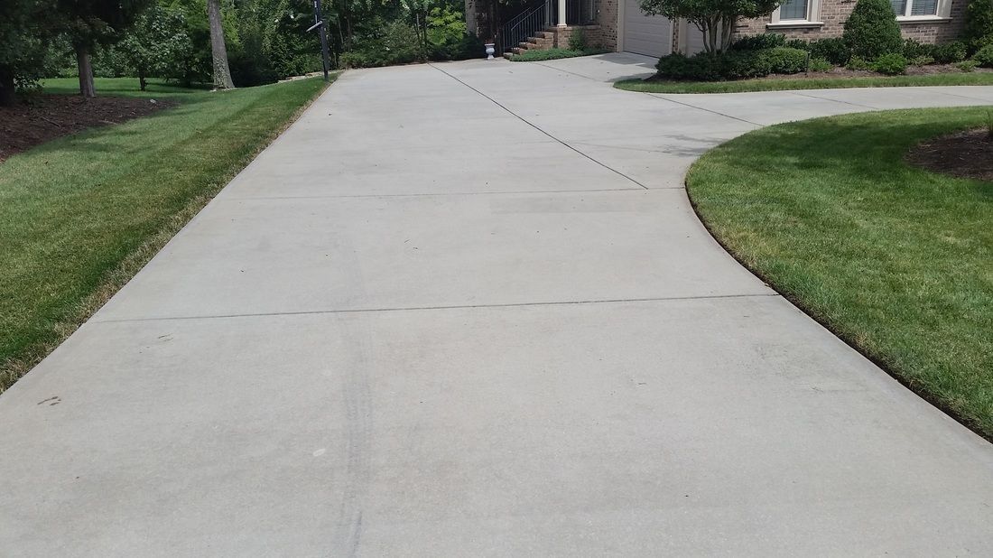 A concrete driveway extends from the foreground toward a residential house, framed by green lawns.