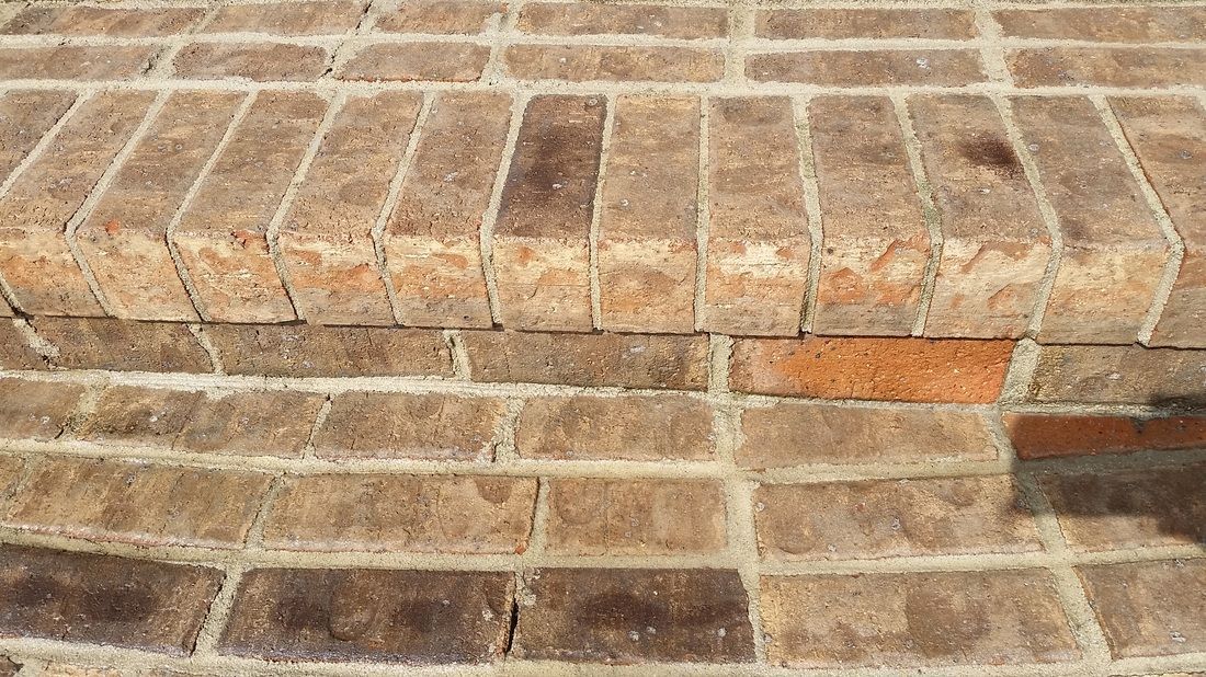 A close-up view of a brick staircase, showing the textured, multicolored brown bricks and mortar joints.