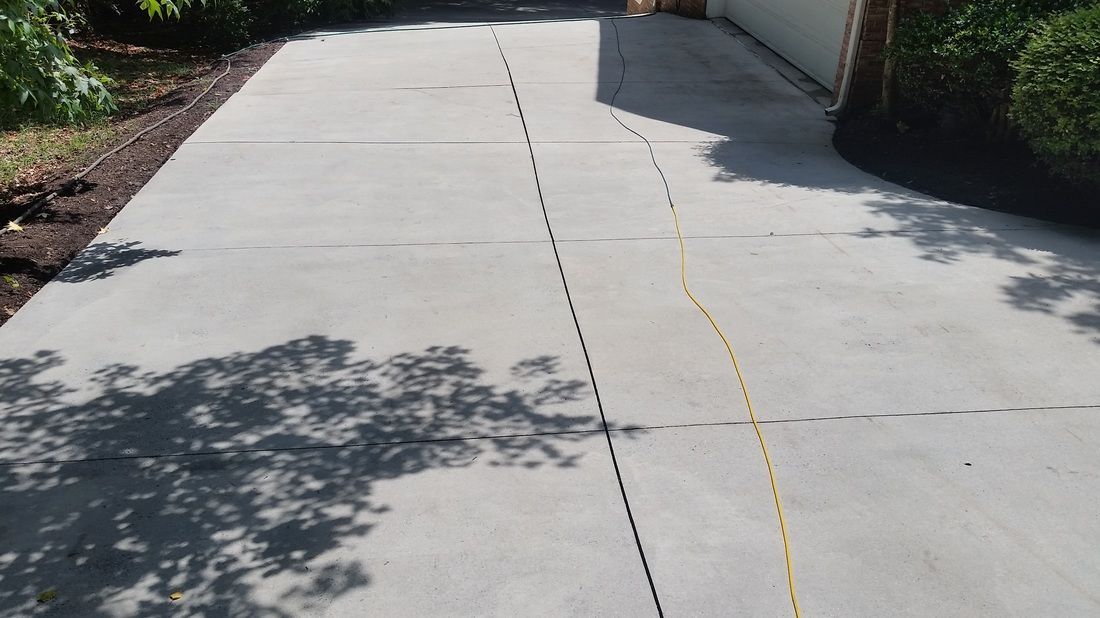 A concrete driveway with a yellow cord running across the surface, extending from the bottom to the upper right.