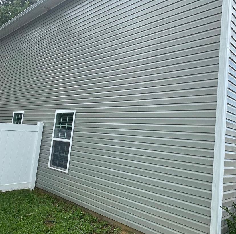 Exterior wall of a house with light grey horizontal vinyl siding, two white-framed windows, and a white privacy fence.