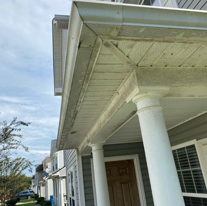 The soffit, fascia, and gutters of a house porch show visible dirt and mildew buildup, with white columns below.