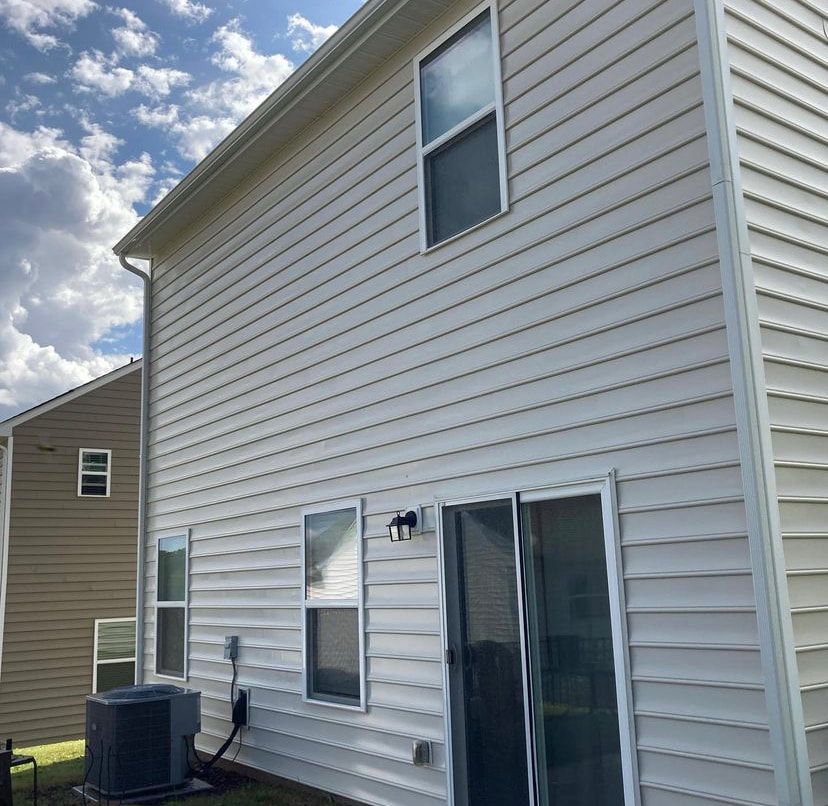 A two-story house exterior with light-colored siding, a sliding glass door, several windows, and an outdoor AC unit.
