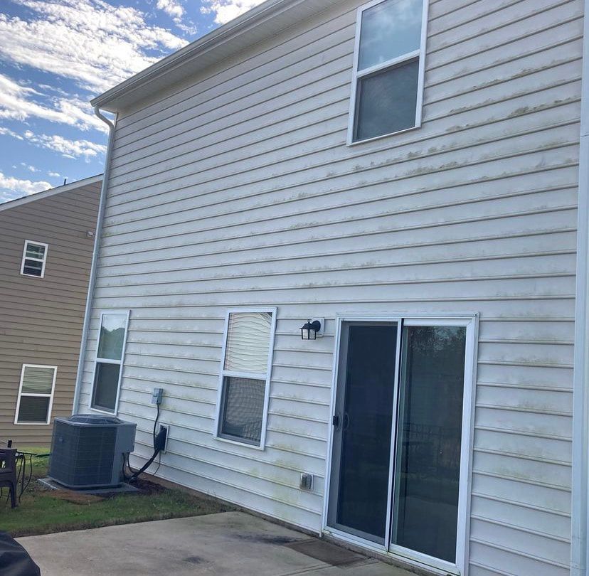 A view of the side of a beige residential building with a sliding glass door, several windows, and an outdoor AC unit.