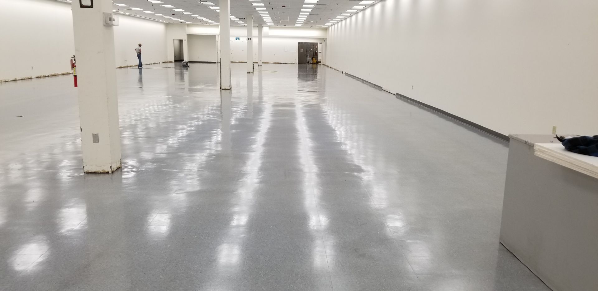 Empty, light-filled commercial space with polished gray floor, white walls, and supporting pillars.