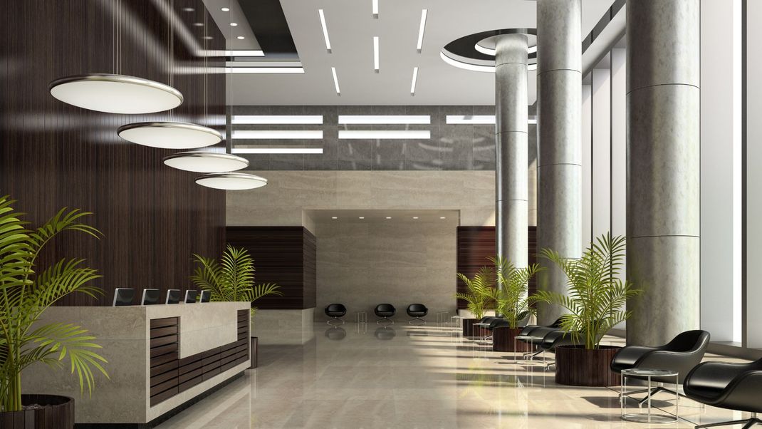Modern office lobby with reception desk, seating area, large windows, and plants.