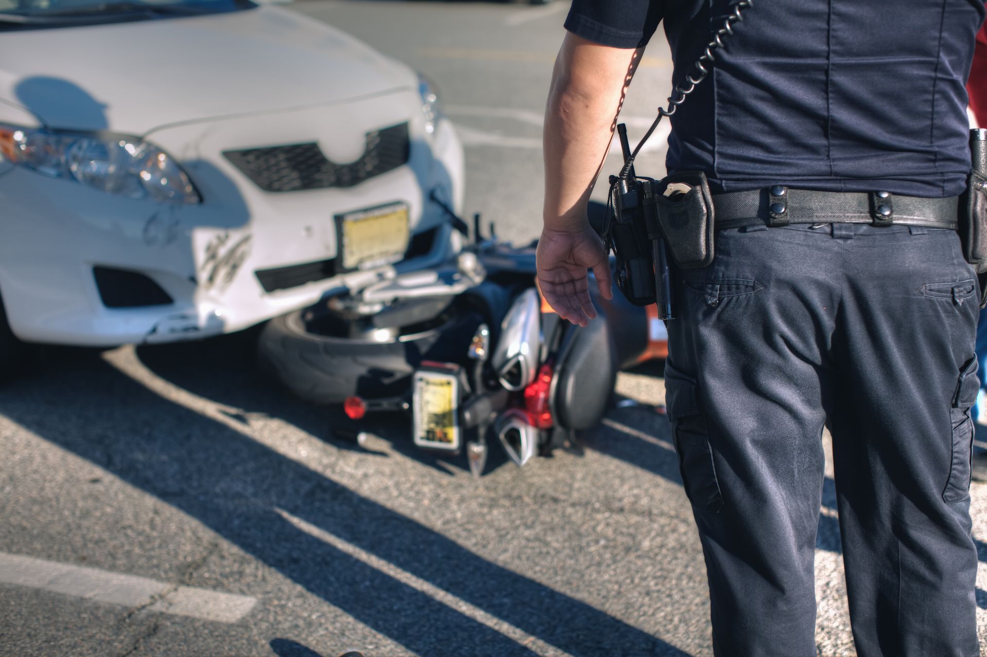 A police officer is standing in front of a car and a motorcycle after a car and motorcycle accident.