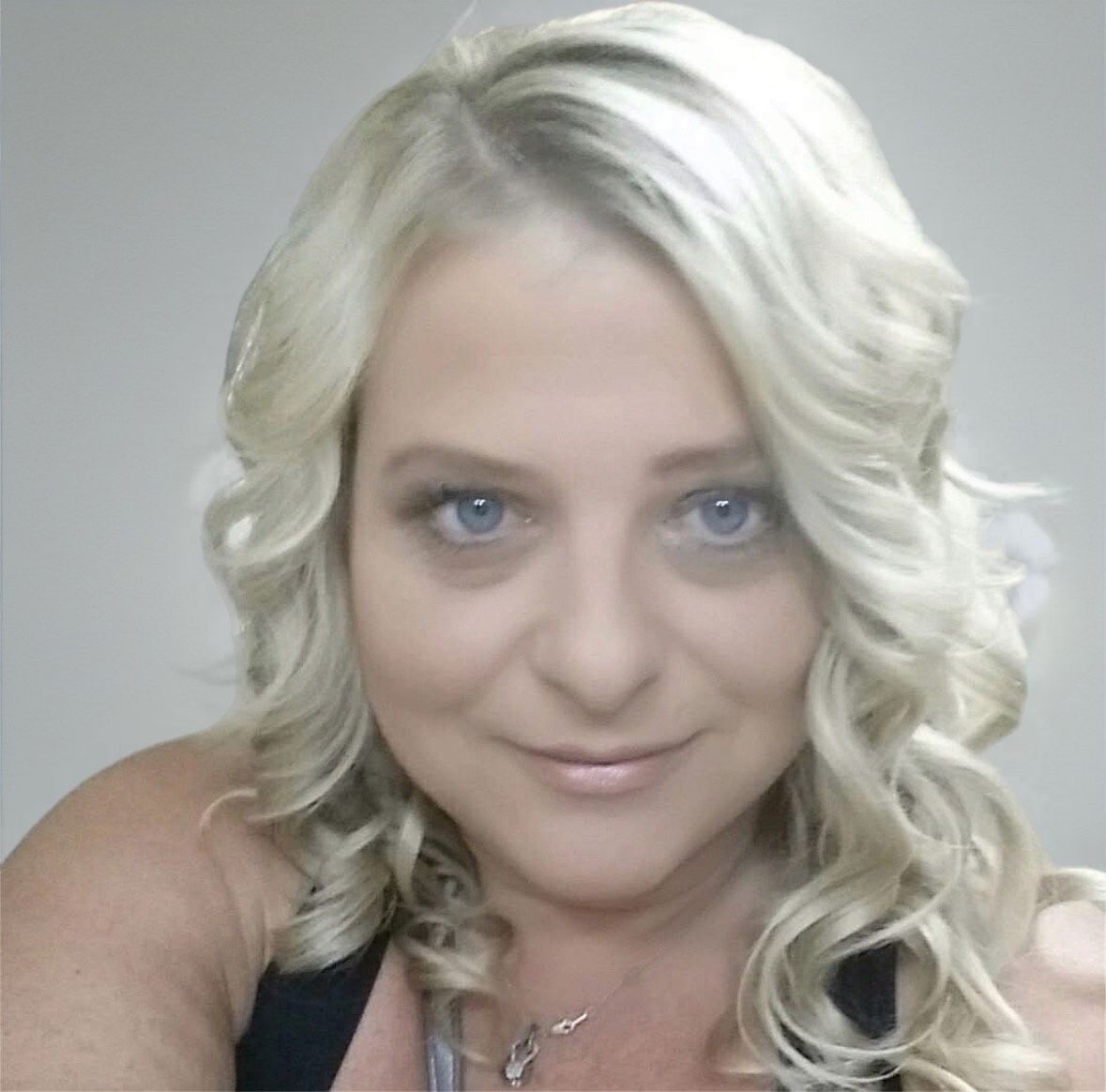 Woman with wavy blonde hair and blue eyes looking at the camera, wearing a black top.