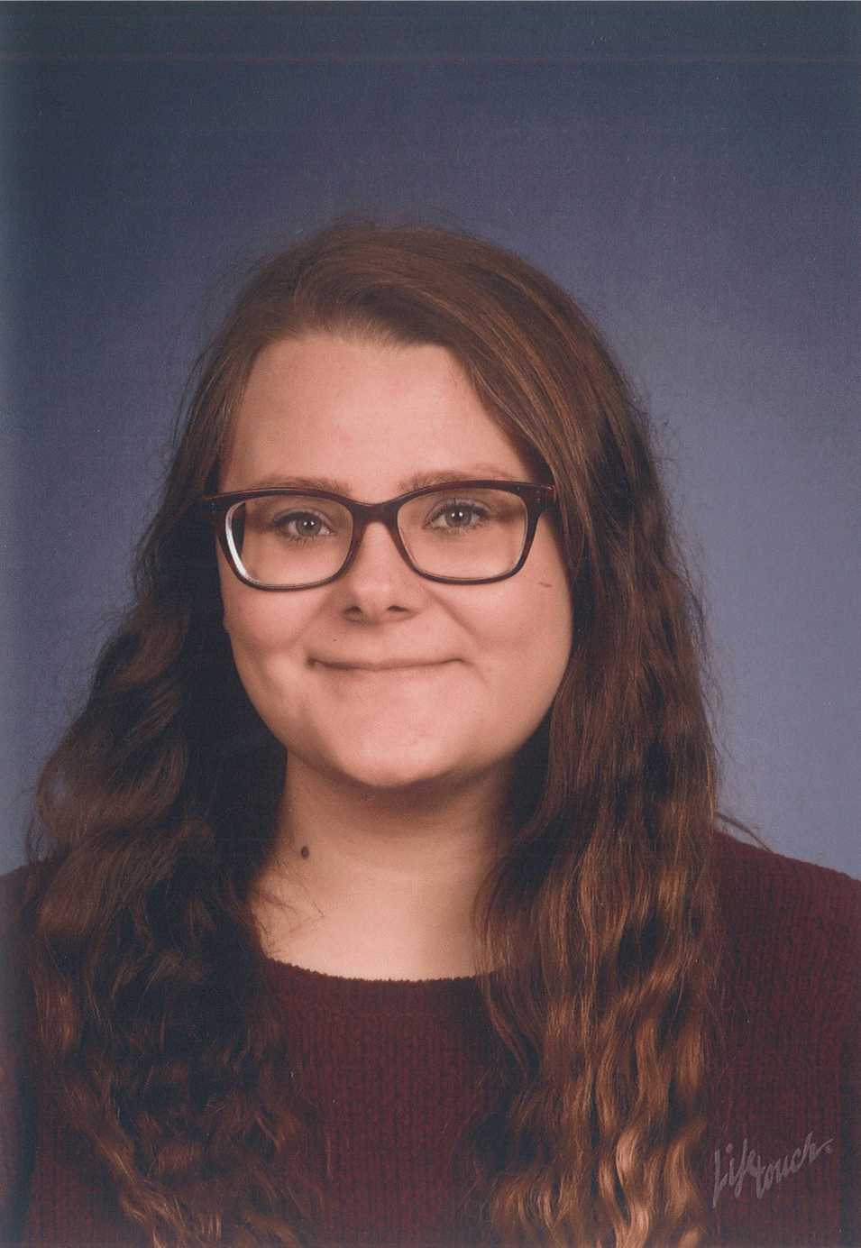 Woman with brown hair and glasses smiling at the camera, wearing a dark red shirt.