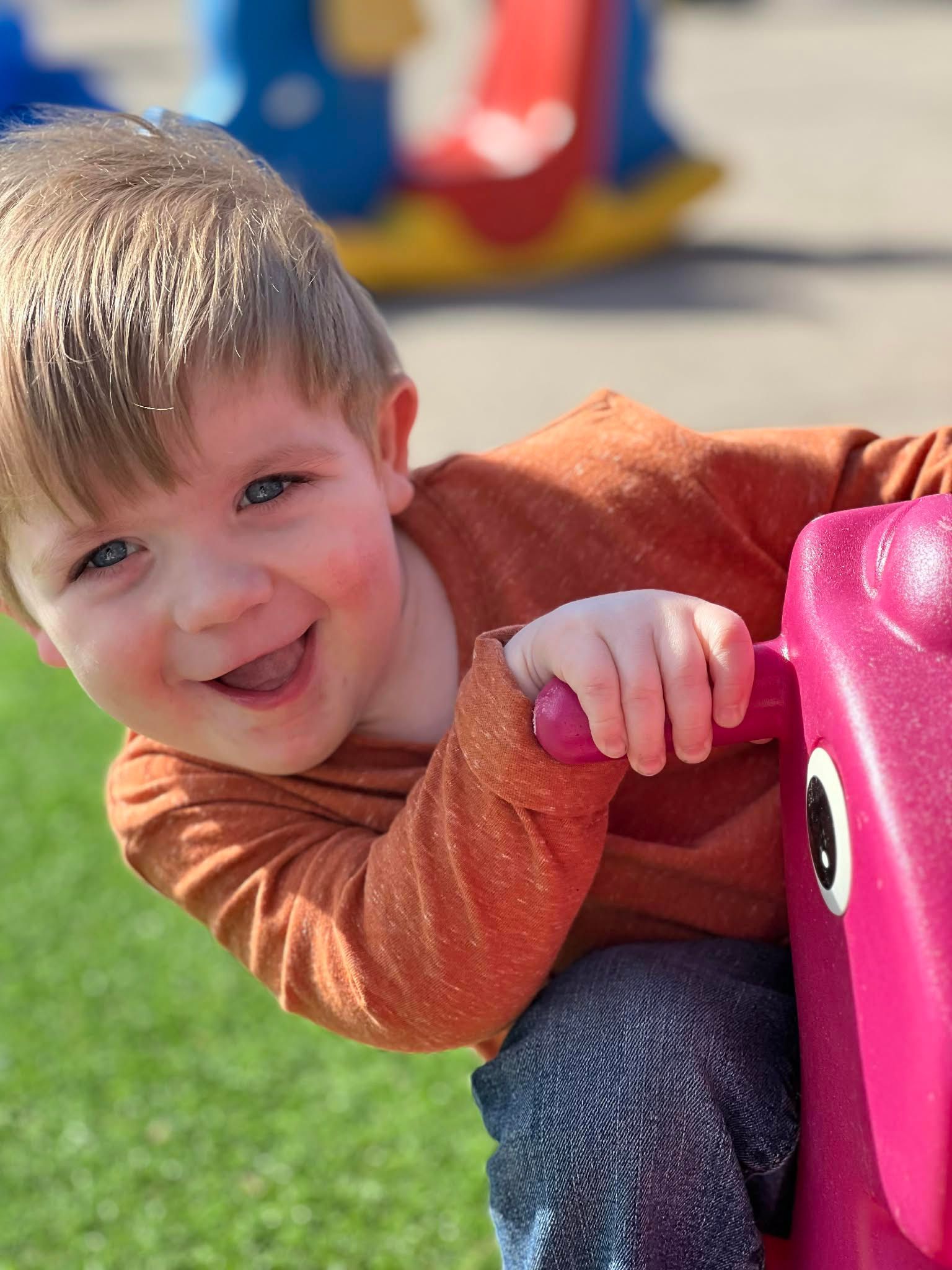 Smiling child in blue shirt and shorts standing in a brightly colored room with toys.