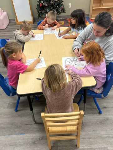 Children and a teacher at a table in a classroom, working on a project.