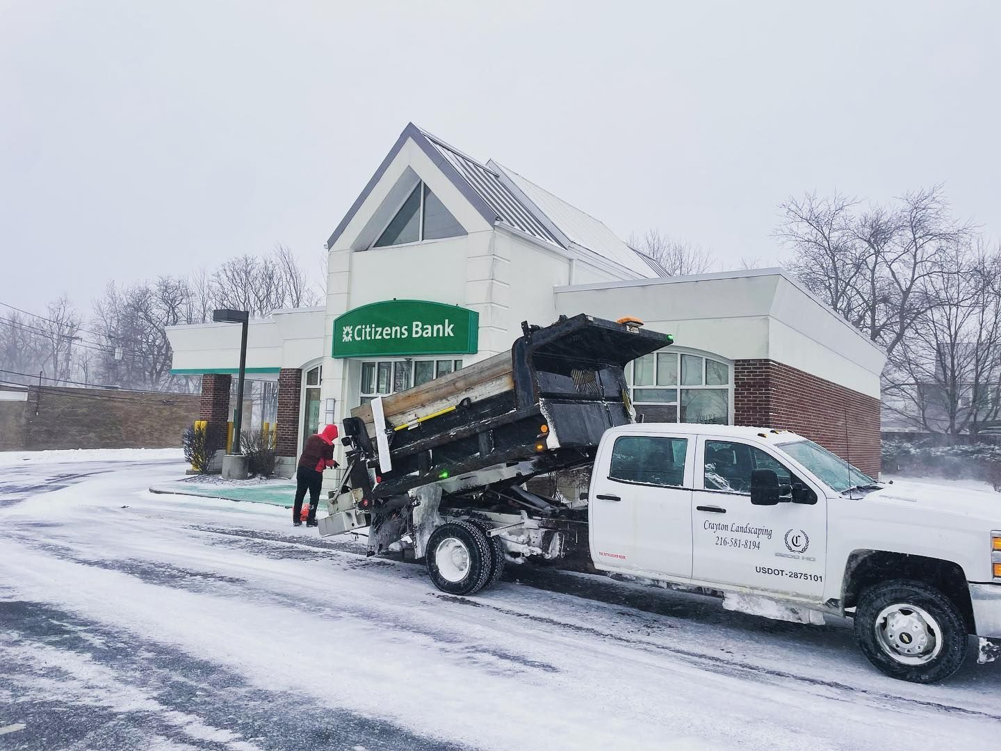 A dump truck is parked in front of a bank in the snow.