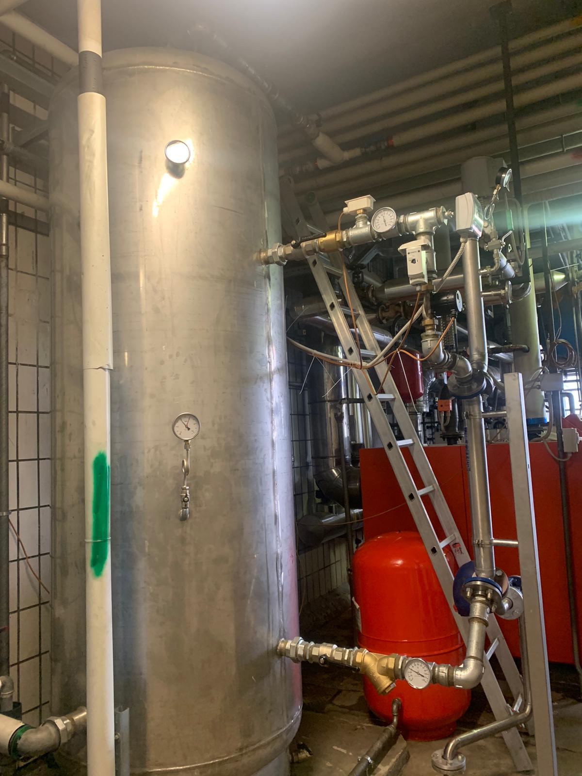 In una stanza, accanto a una scala, si trova un grande serbatoio in acciaio inossidabile.