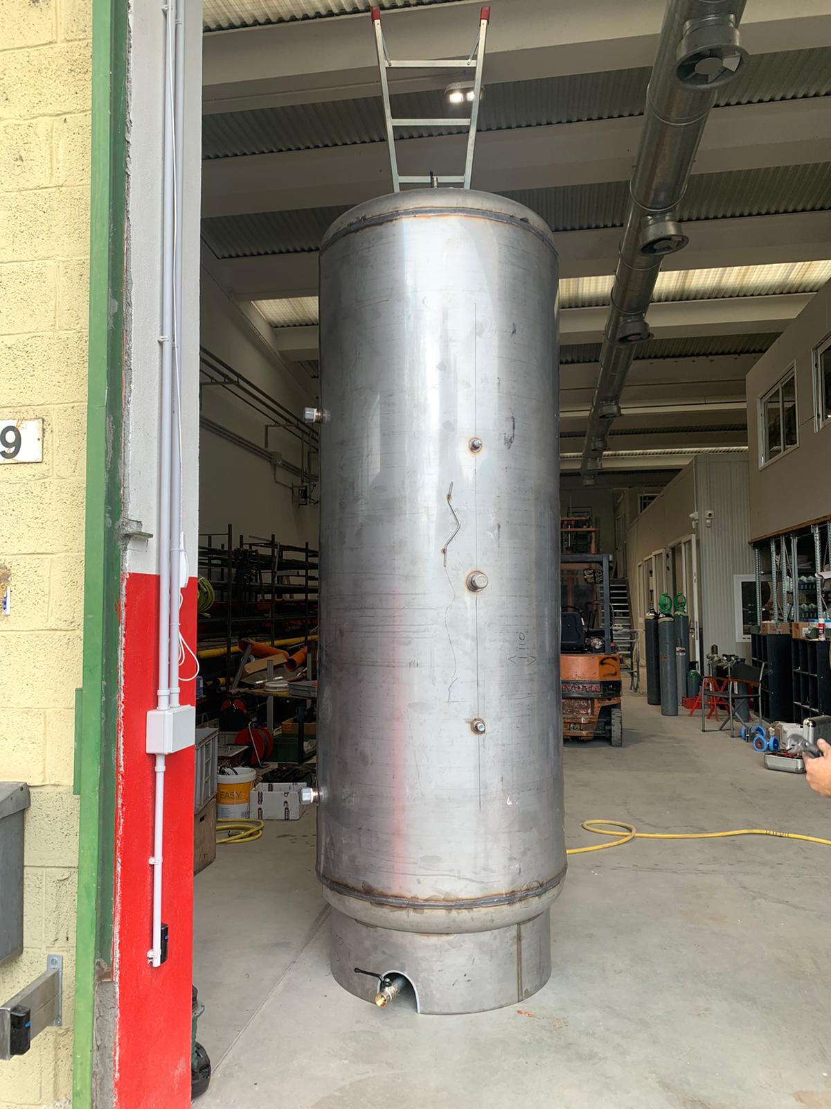 In un magazzino c'è un grande serbatoio in acciaio inossidabile con una scala attaccata.