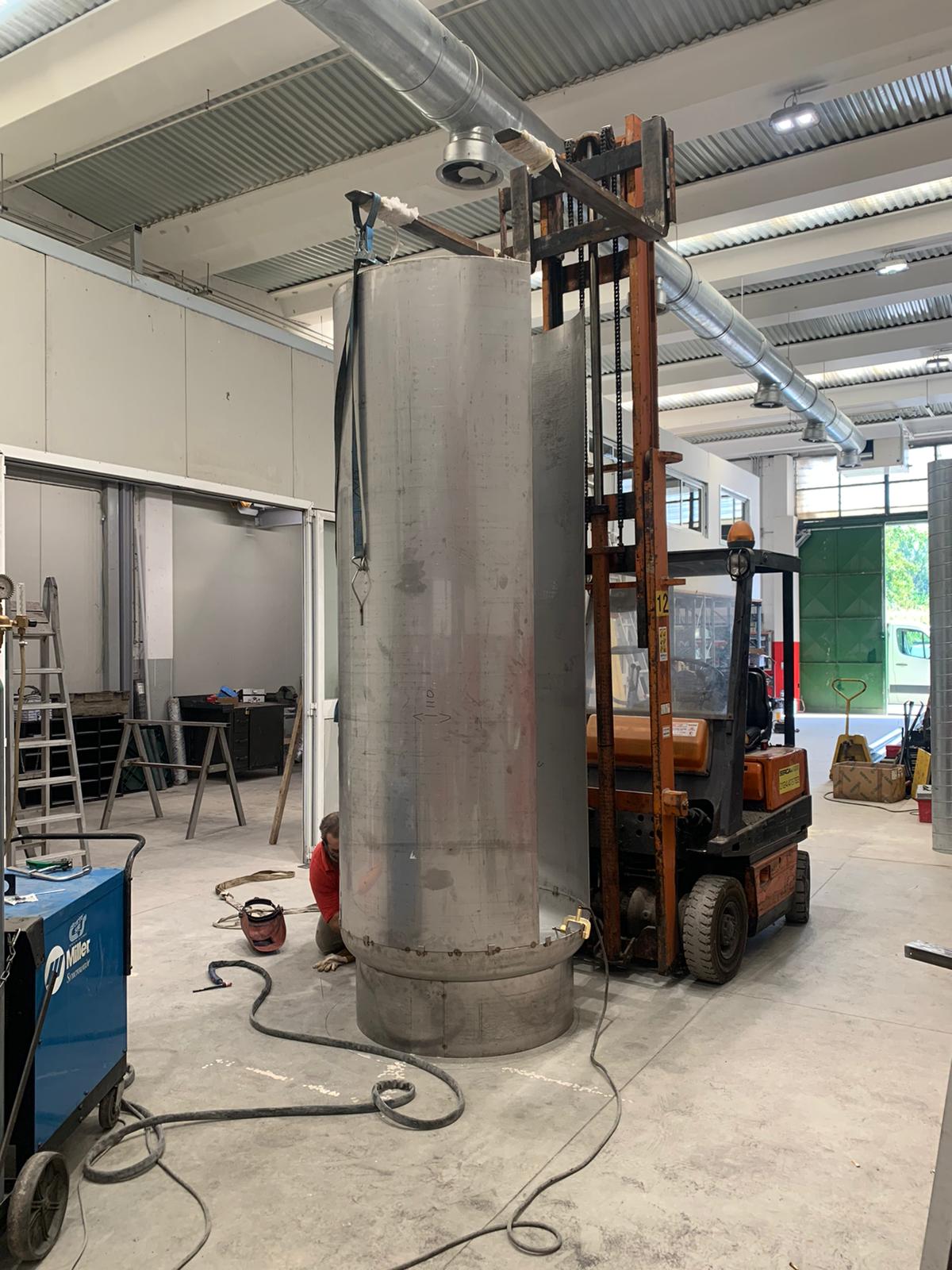Un carrello elevatore sta sollevando un grande oggetto metallico in una fabbrica.