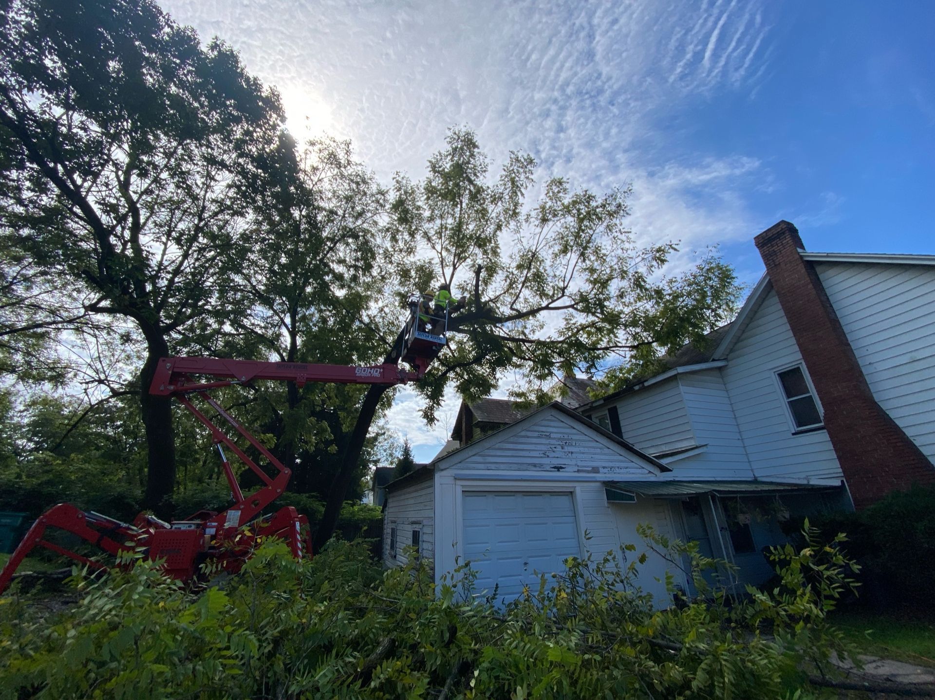 A man is cutting a tree in front of a house.