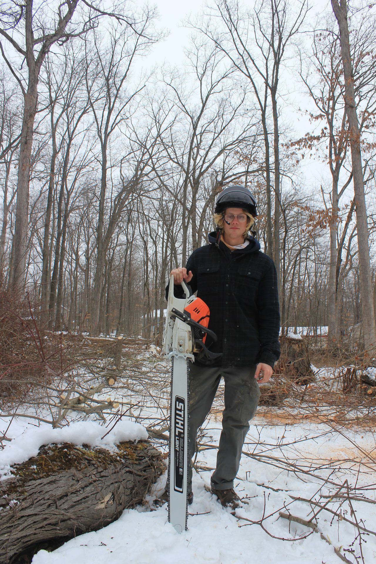 A man is standing in the snow holding a chainsaw.