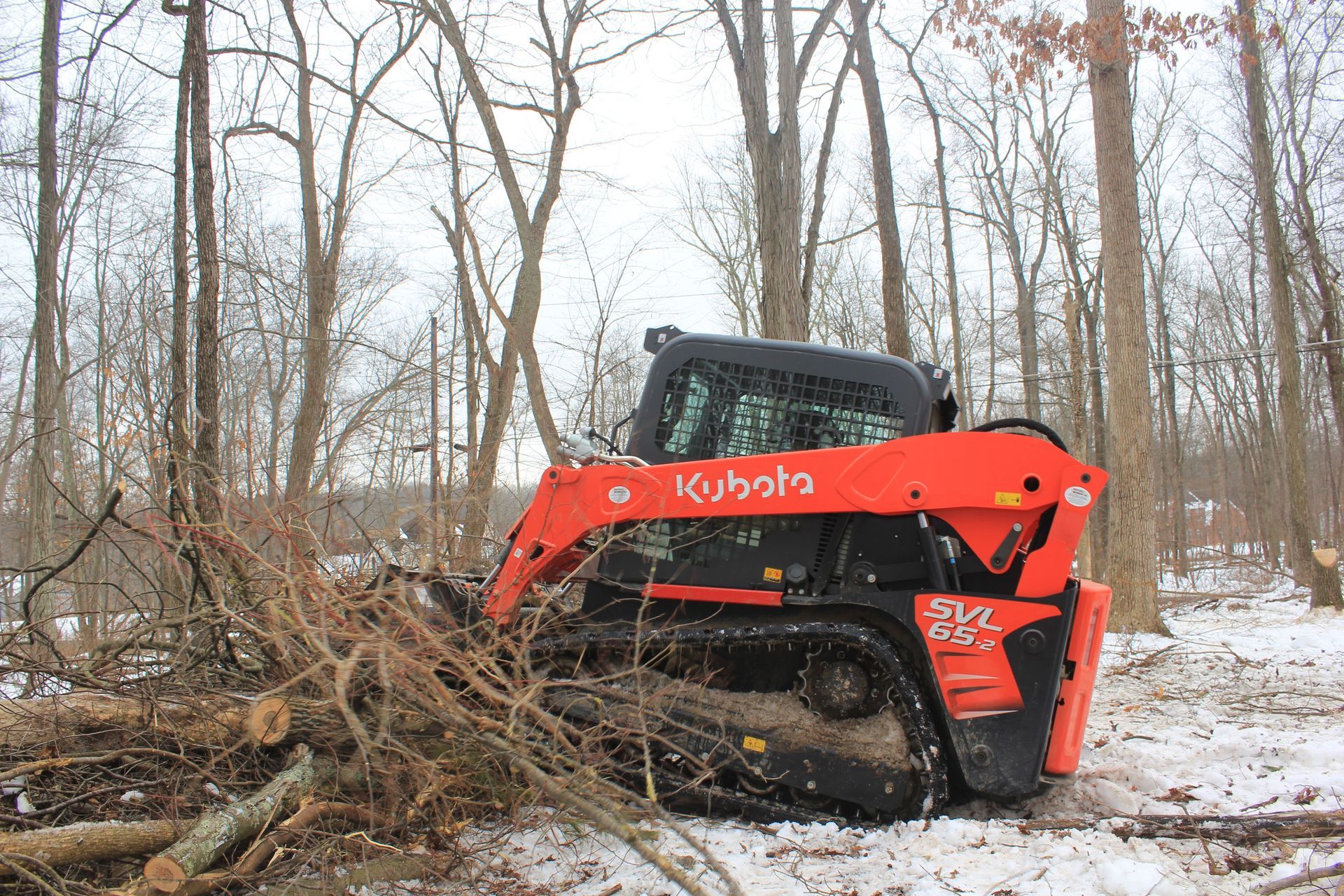 A red and black kubota skid steer is driving through a snowy forest.