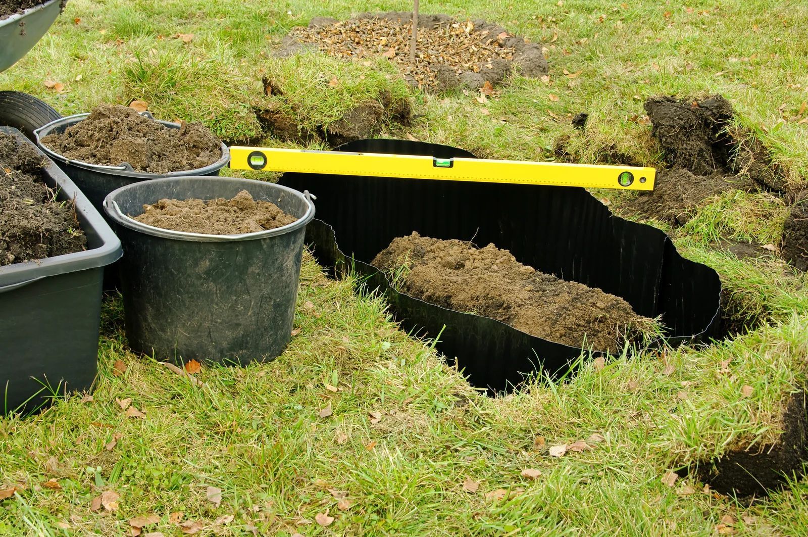 A garden being dug, a level is used. Buckets of dirt are beside the hole.