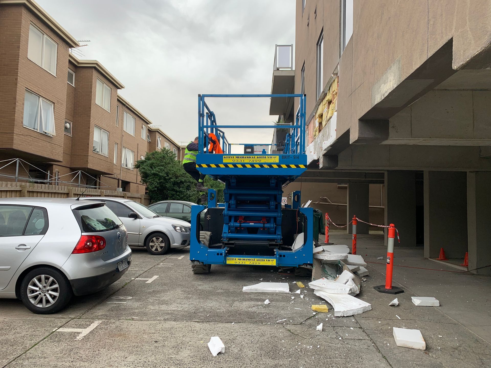 A blue scissor lift is parked in a parking lot next to a building.