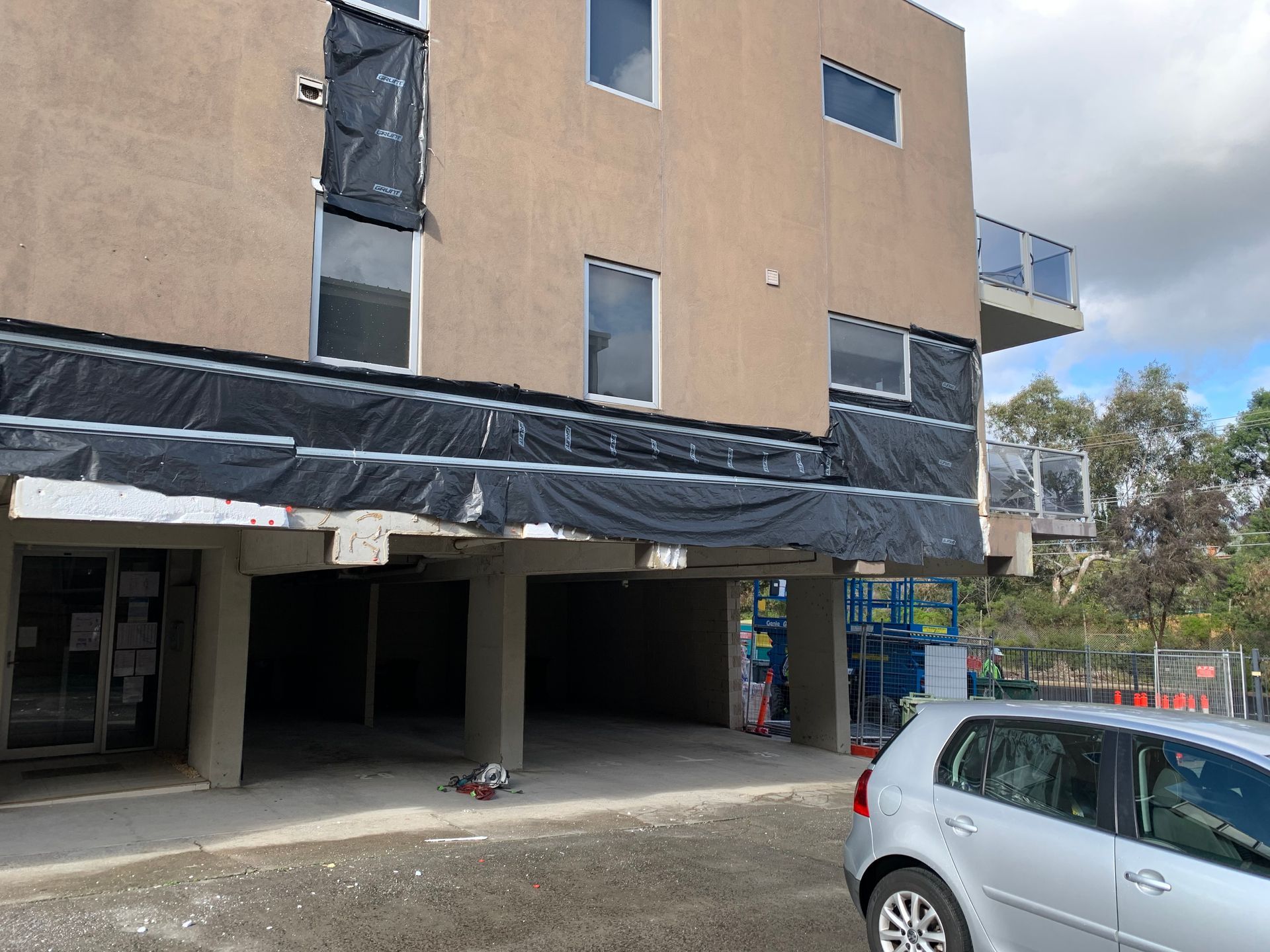 A silver car is parked in front of a building under construction.