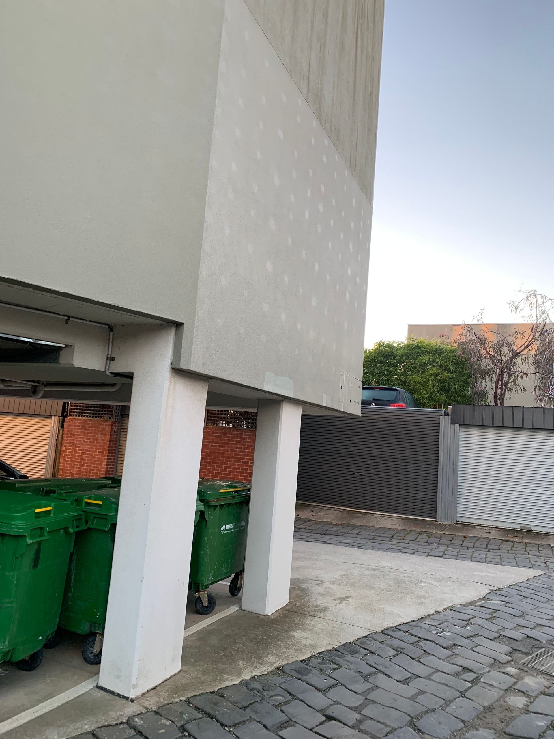 Two green garbage cans are parked in front of a building