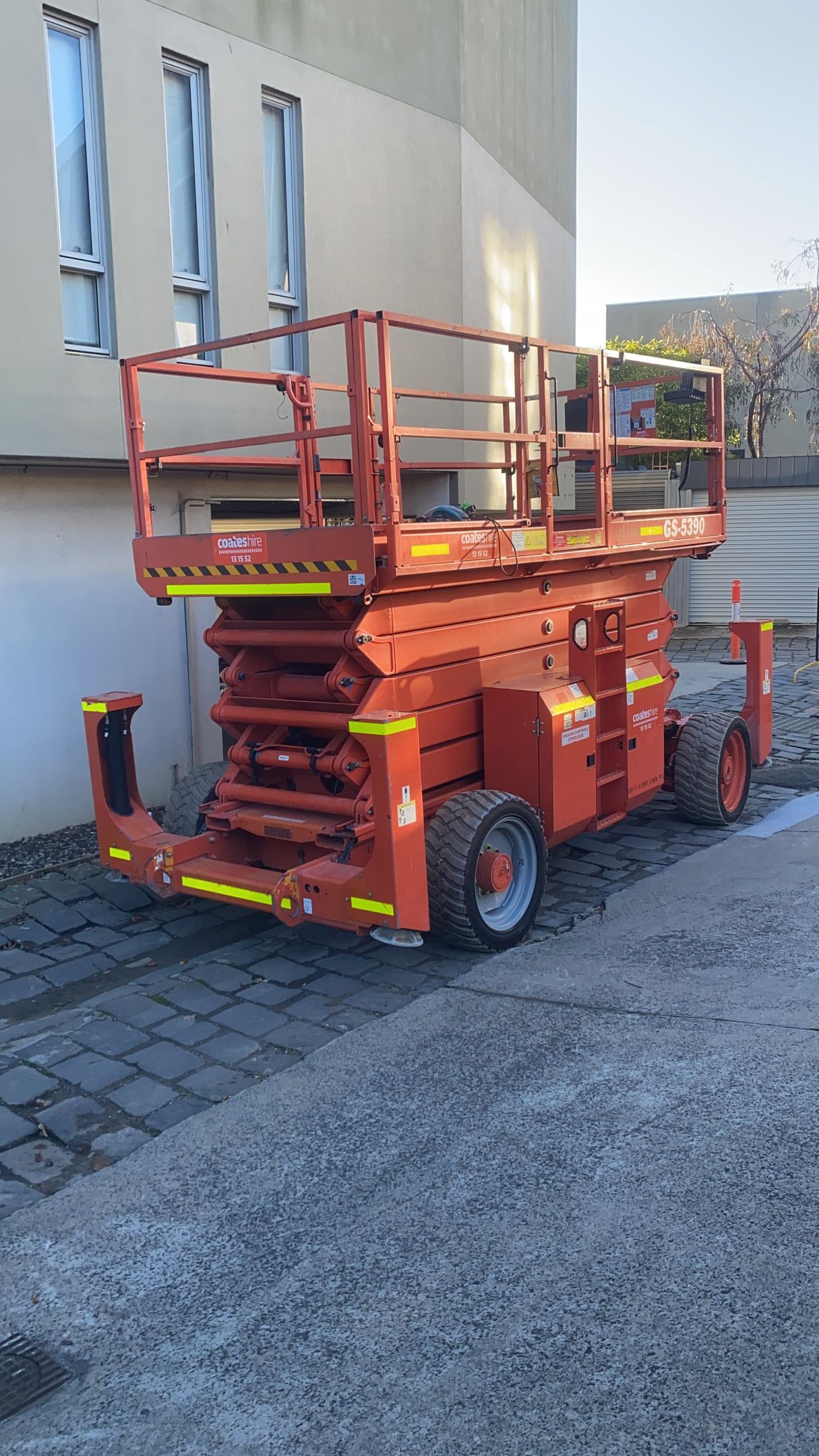 A red scissor lift is parked in front of a building.