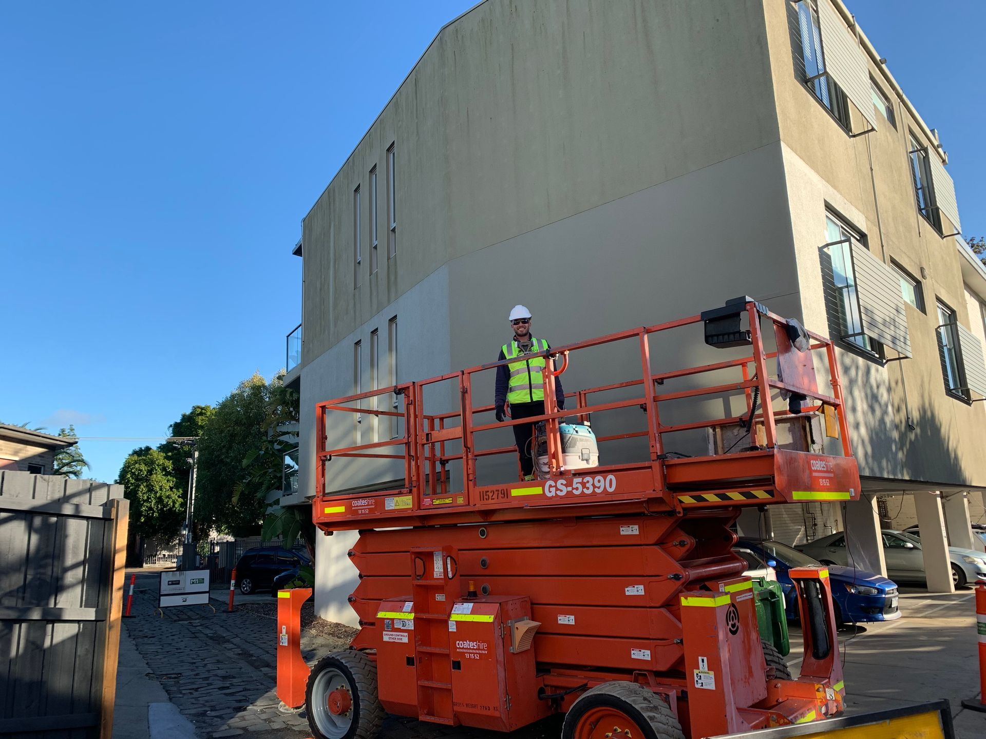 A man is standing on a scissor lift in front of a building.