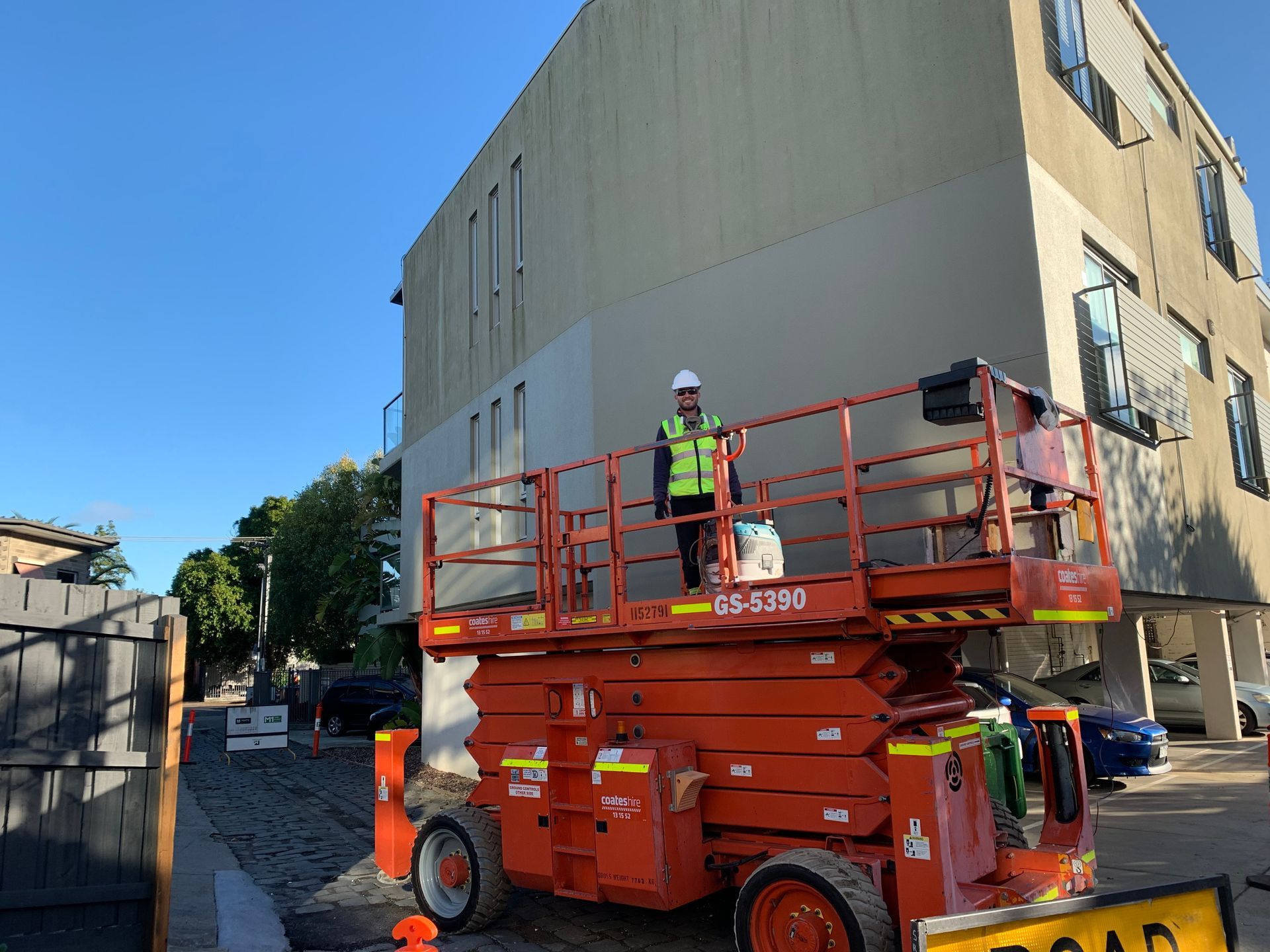 A man is standing on a scissor lift in front of a building.