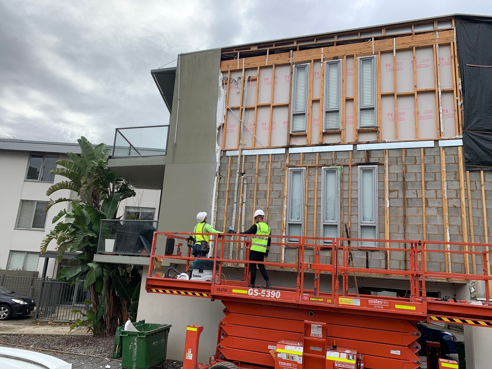 Two construction workers are working on the side of a building.