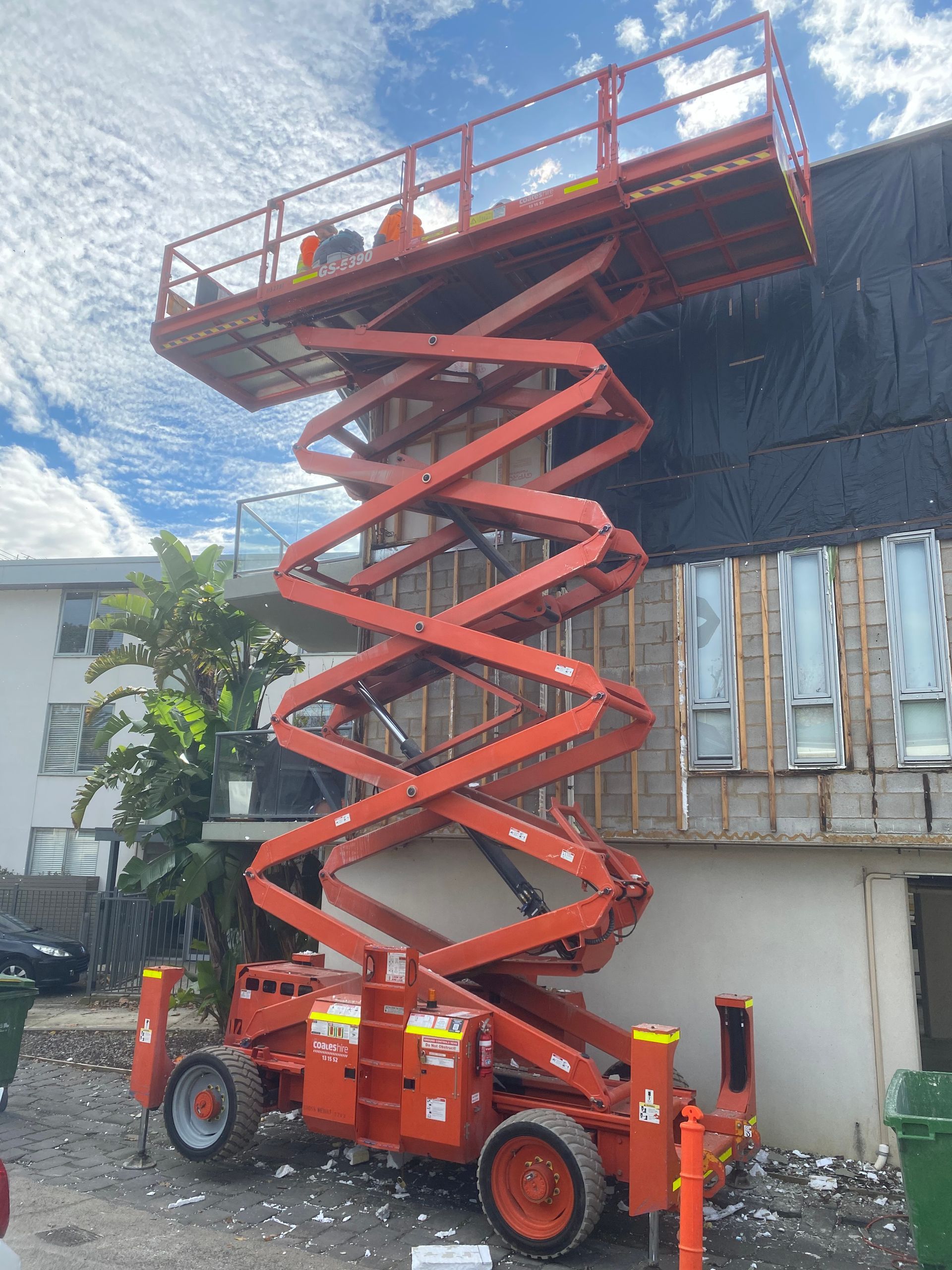 An orange scissor lift is parked in front of a building.