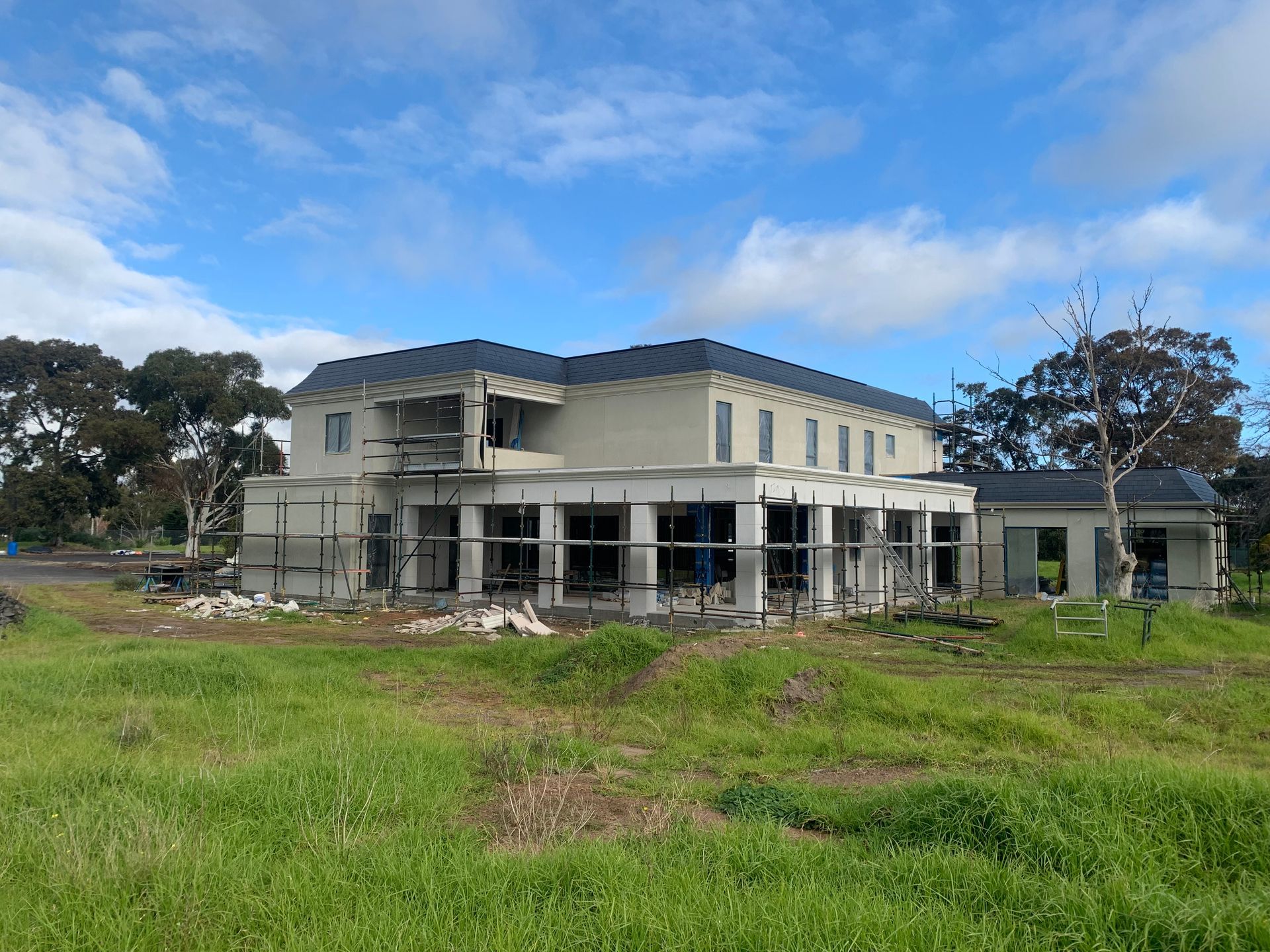 A large house is being built in a grassy field.