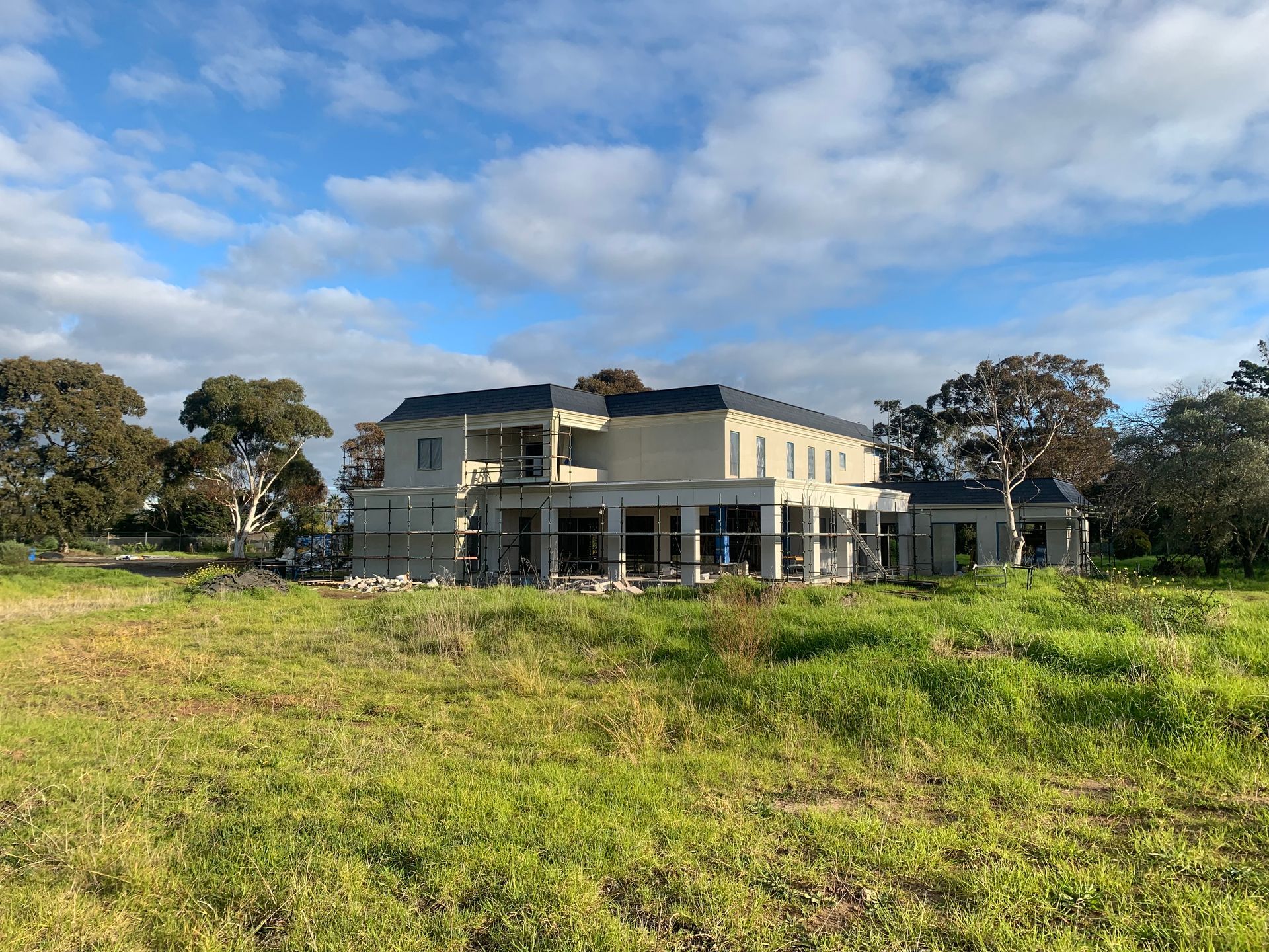 A large house is being built in a grassy field.