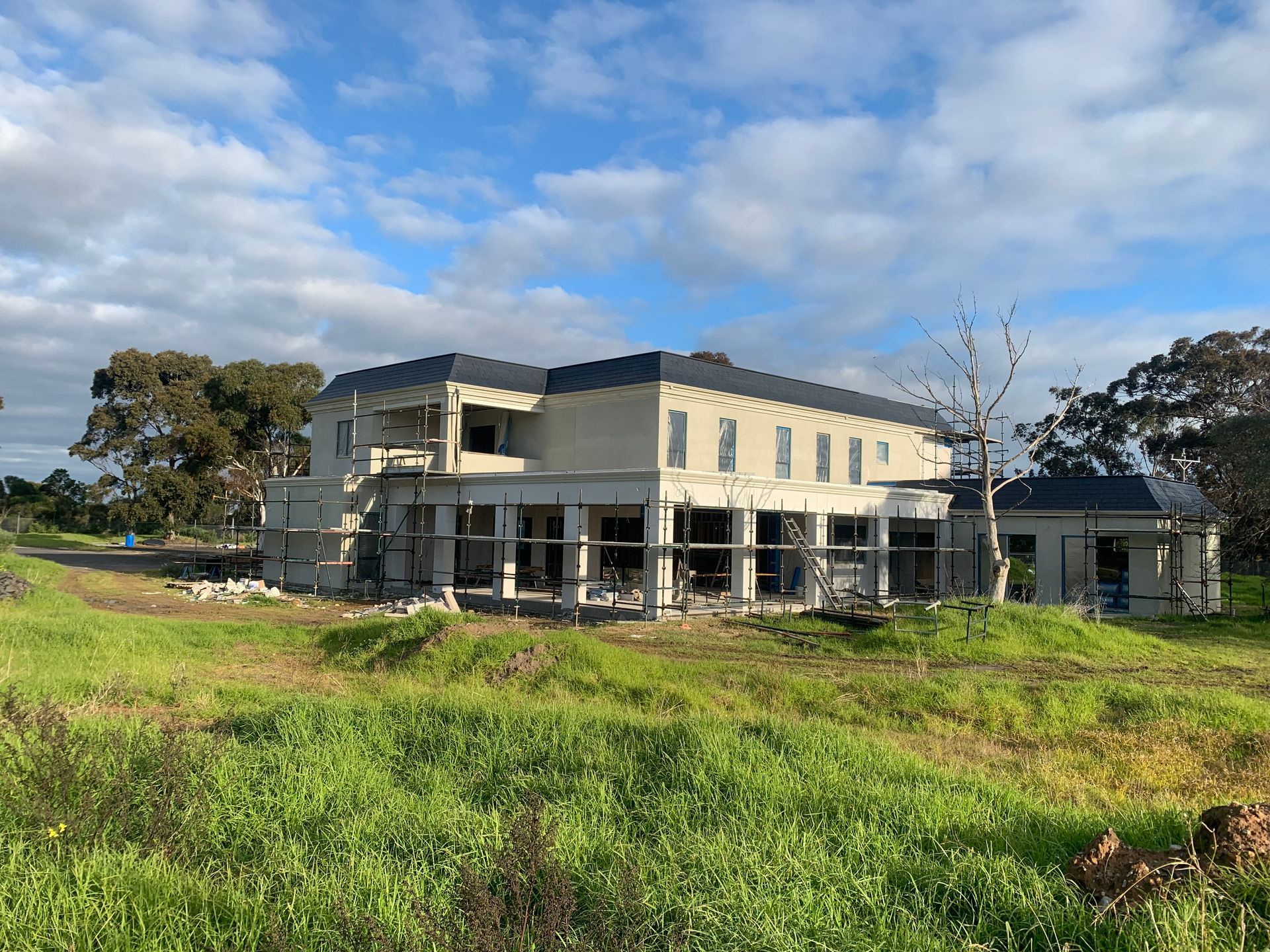 A large house is being built in a grassy field.