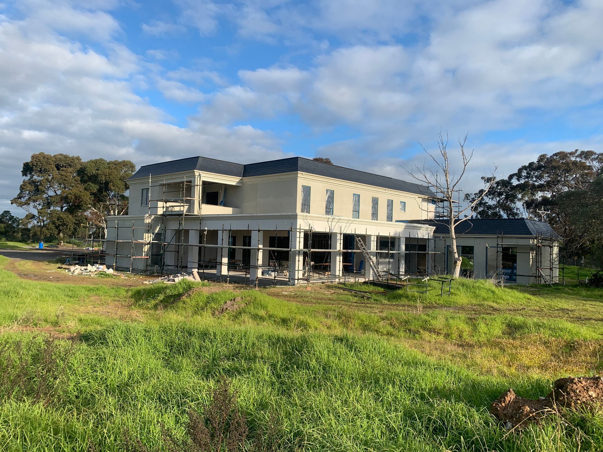 A large house is being built in a grassy field.