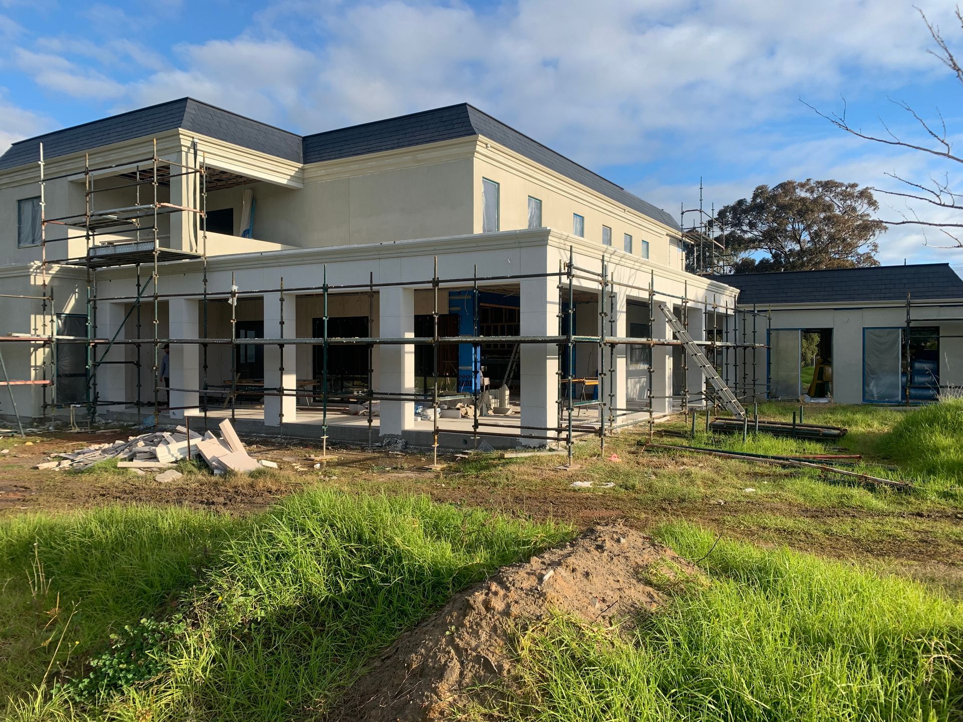 A large house is being built in a field with scaffolding around it.