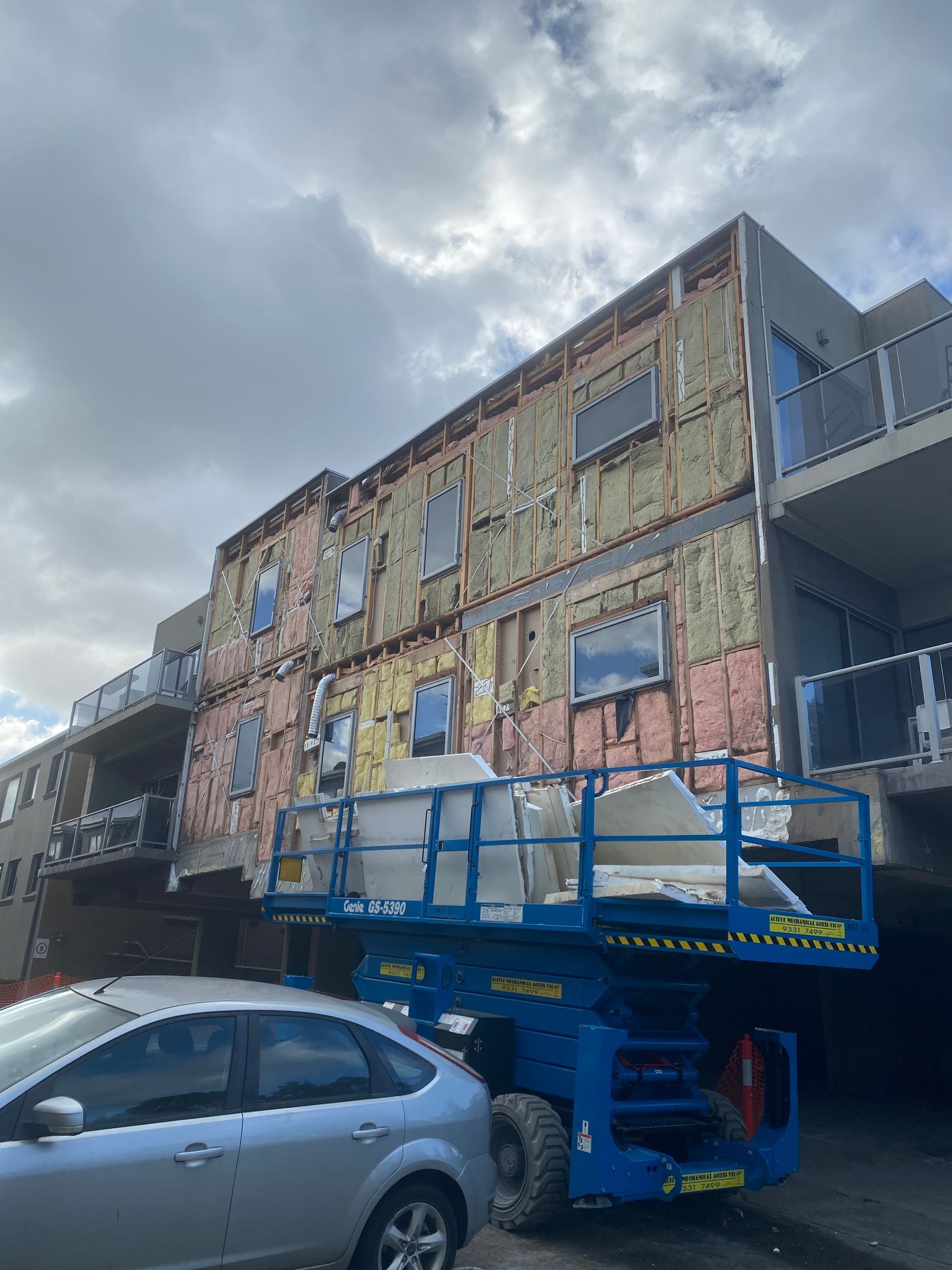 A car is parked in front of a building under construction.