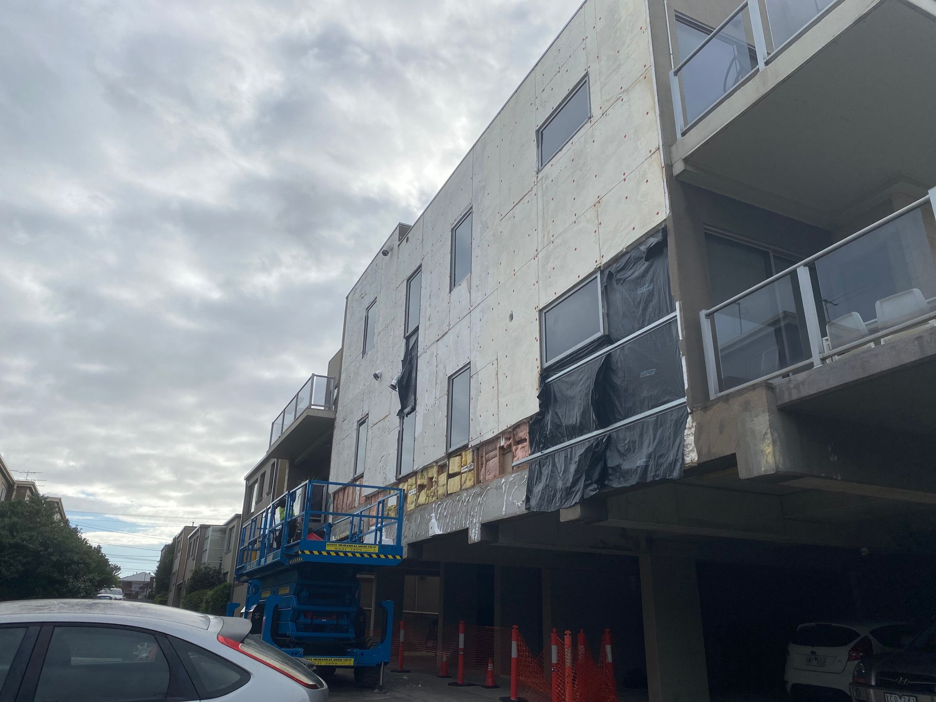 A white car is parked in front of a building under construction.