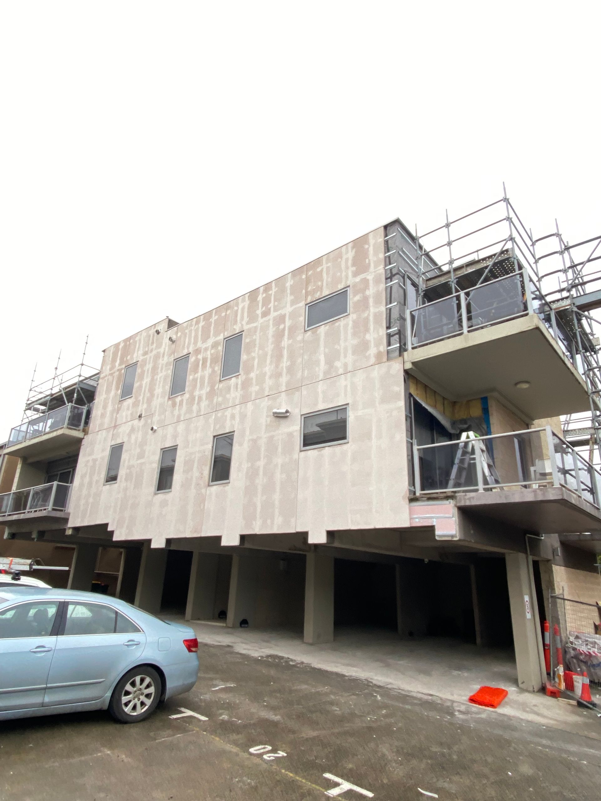 A car is parked in front of a building under construction.
