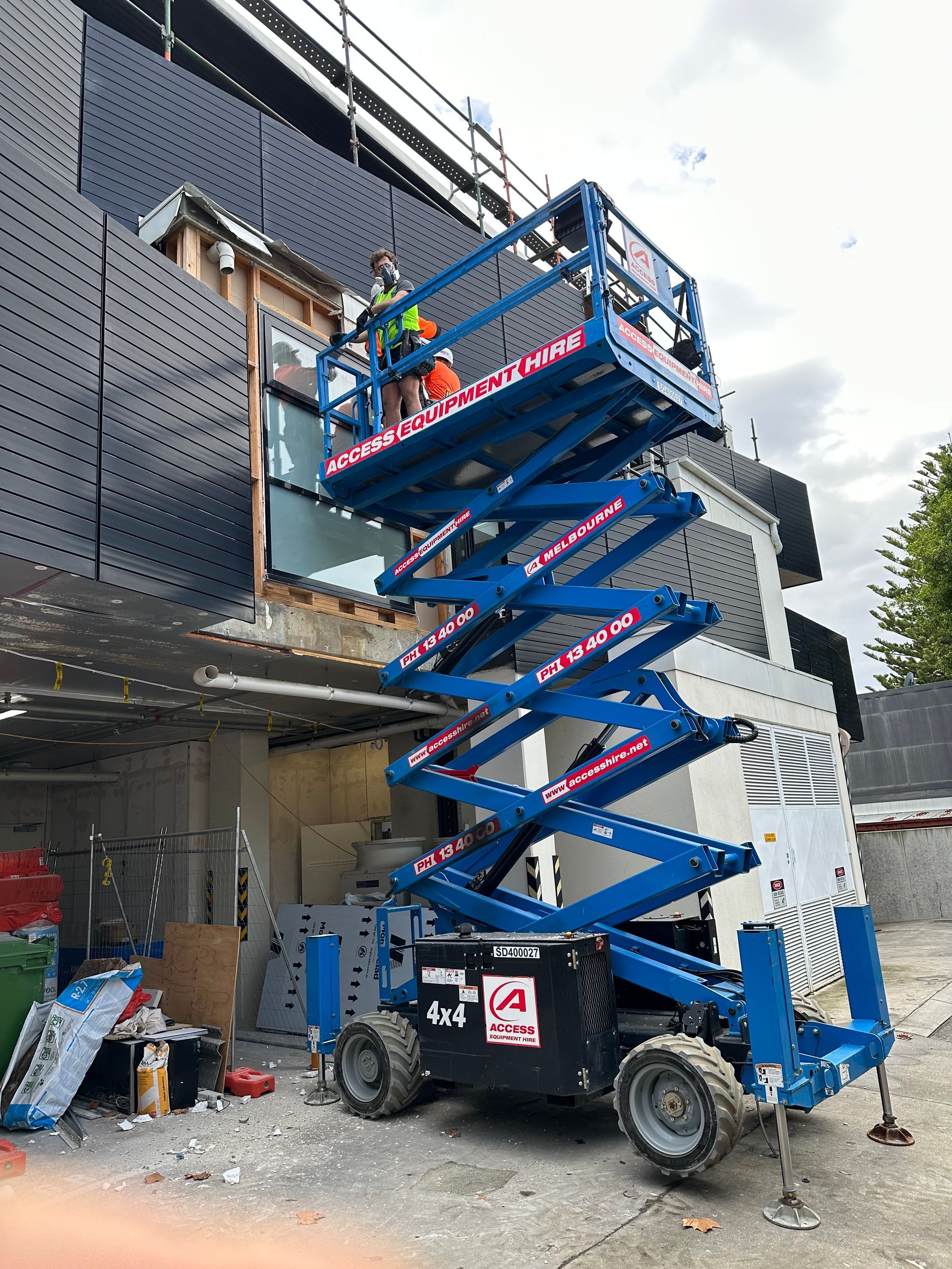 A man is standing on a scissor lift in front of a building.