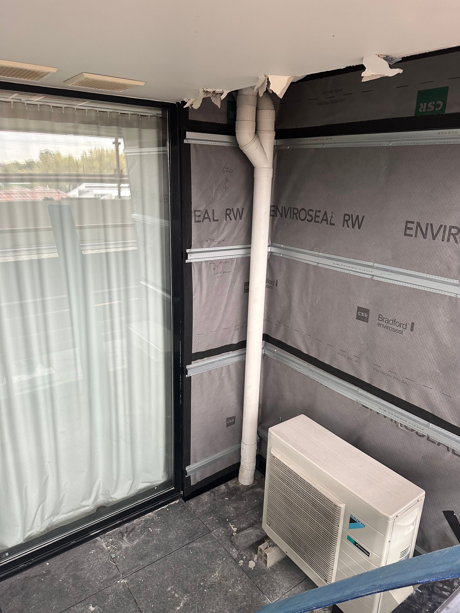 An air conditioner is sitting on a balcony next to a window.