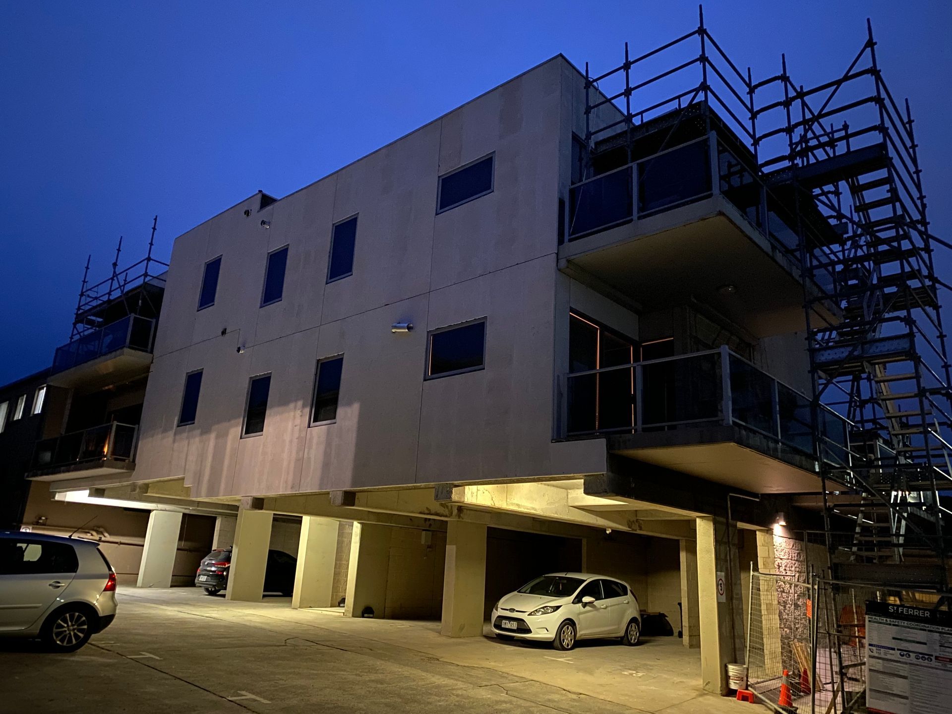 A building under construction with cars parked in front of it at night.