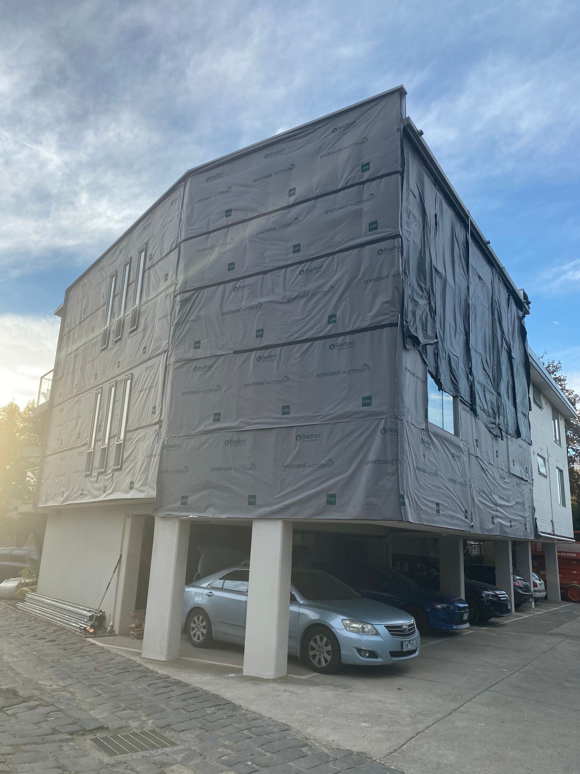 Two cars are parked in front of a building that is covered in tarps.