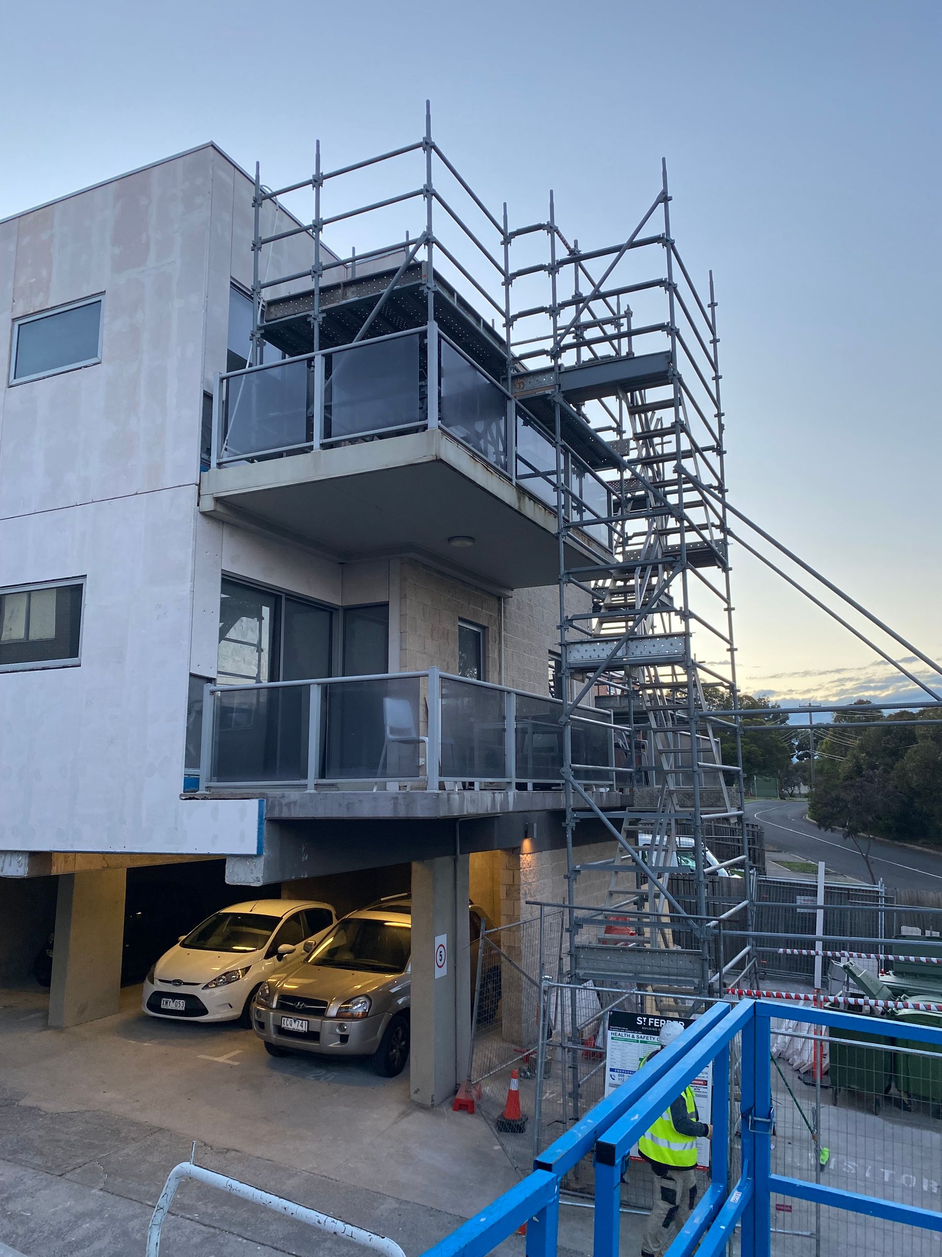A building with scaffolding on top of it and cars parked in front of it