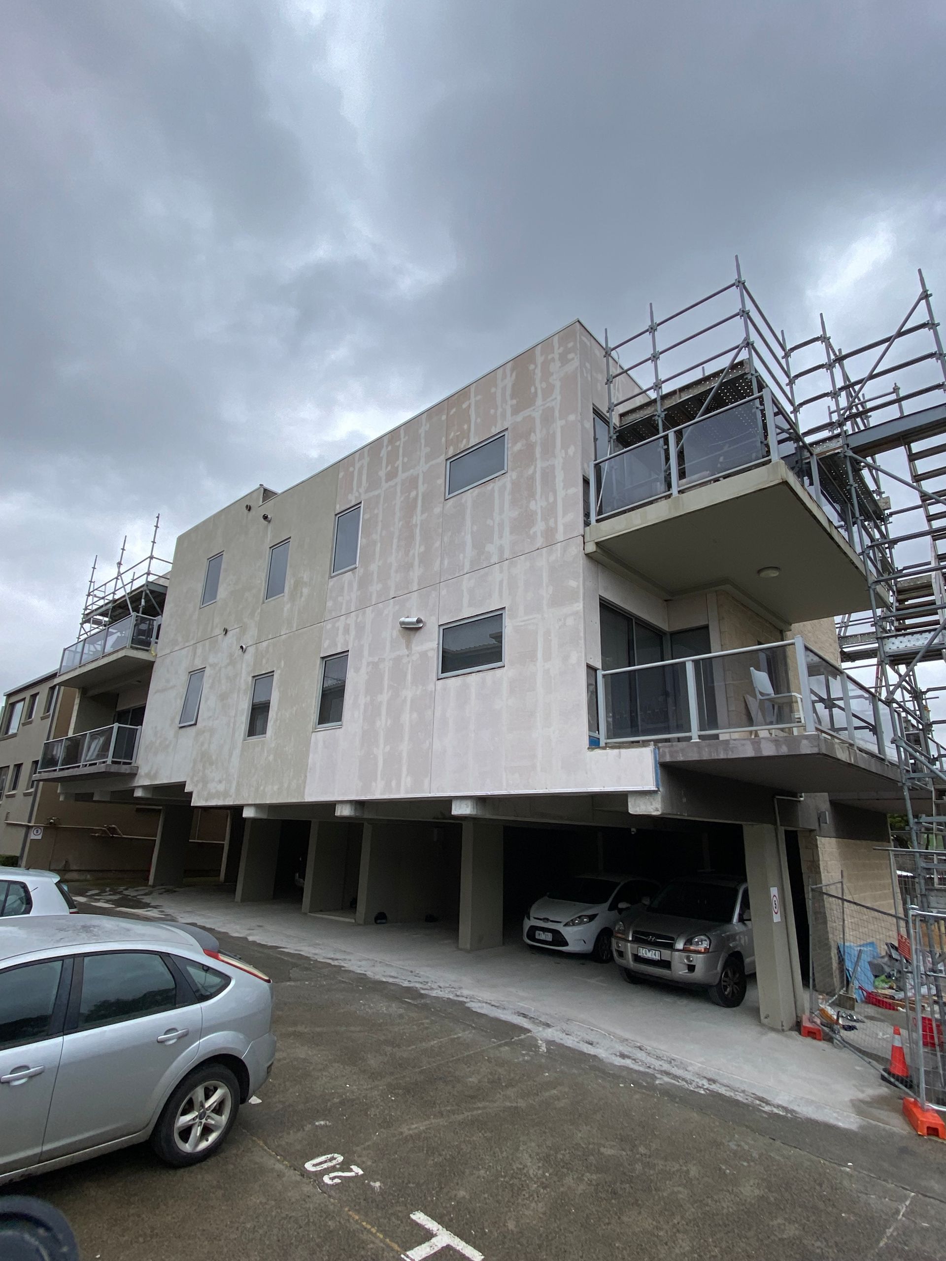 A building under construction with cars parked in front of it.