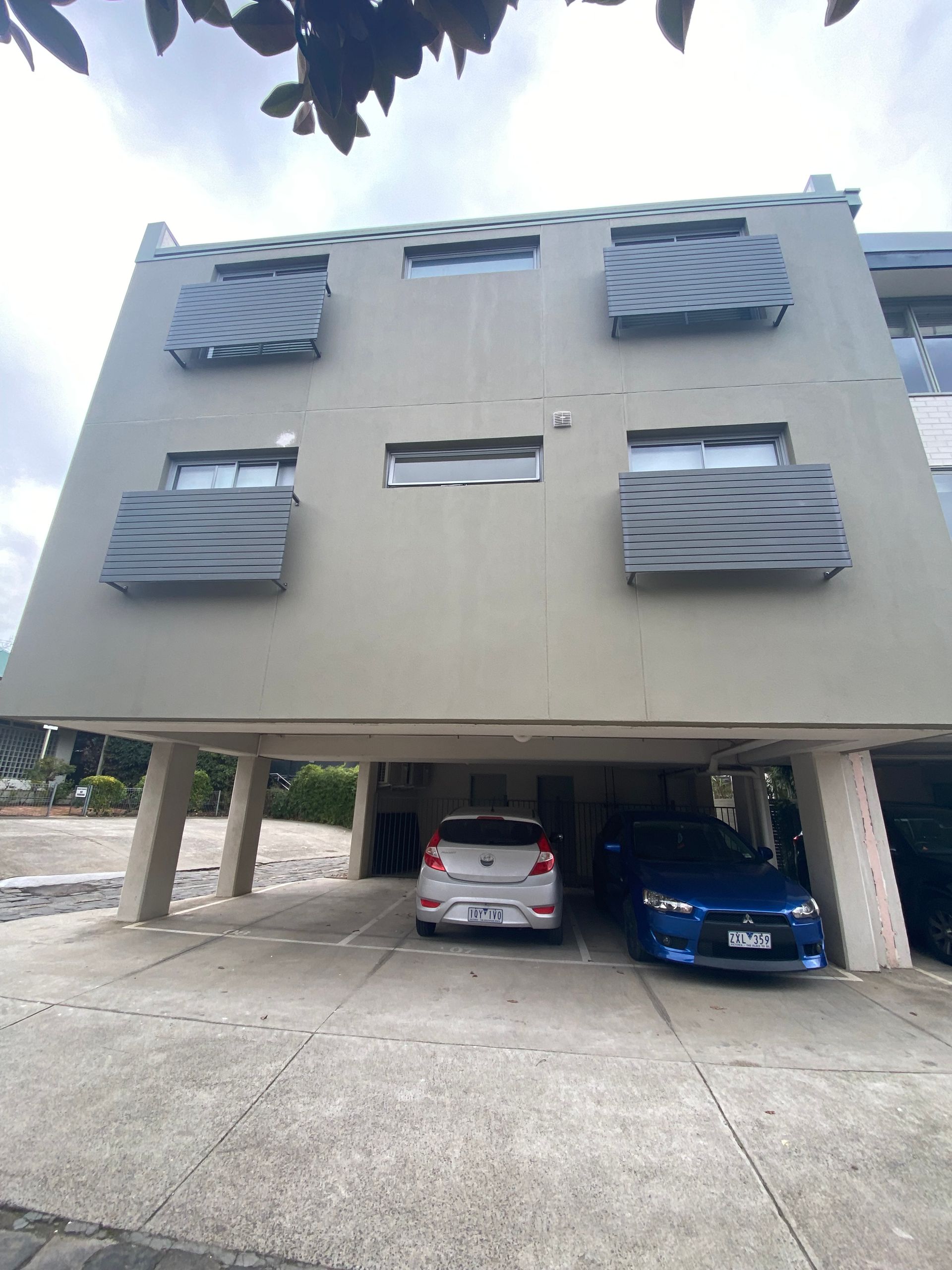 Two cars are parked in front of a building with balconies