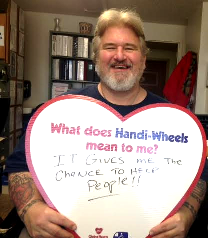 A male holding a heart with these written words: What does Handi-Wheels mean to me? It gives me the chance to help people!!