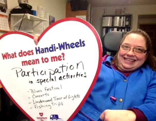 A female holding a heart with these written words: What does Handi-Wheels mean to me? Participation in special activities.